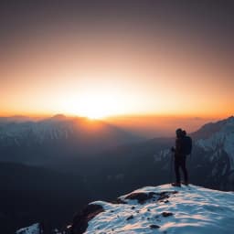 a hiker standing on a ridge overlooking snow-covered peaks at sunrise